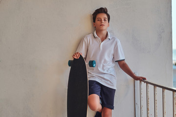 Young skater boy dressed in t-shirt and shorts leaning on the wall.