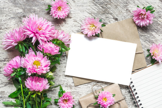 Creative layout made with pink aster flowers, blank greeting card, notepad and gift box on white wooden background