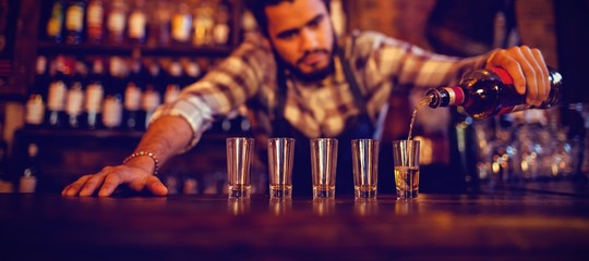 Waiter pouring tequila into shot glasses at counter 