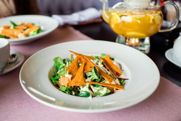 Caesar salad with chicken, greens and crispy chips on the table. Business lunch with a beautiful pineapple-orange tea in a glass teapot.