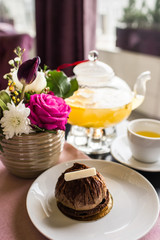 Chocolate truffle cake dessert with white chocolate. Pineapple tea with a transparent glass teapot. Citrus vitamin tea and a beautiful bouquet of flowers with roses, daisies and tulips on the table.