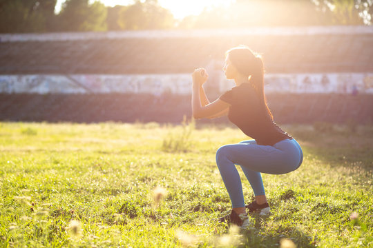 Fitness tanned girl in sport clothes crouching at the stadium in rays of sun. Space for text