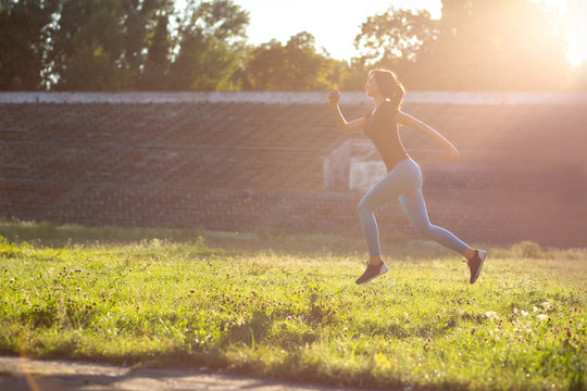 Slender athletic woman running at the stadium in the sunset. Space for text