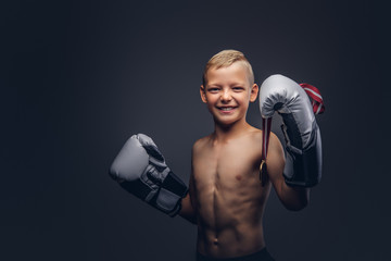 Joyful shirtless boy boxer in boxing gloves holds a golden medal posing in a studio.