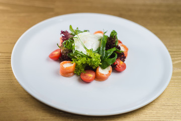 Rolls of salmon with cheese and salad on a white plate