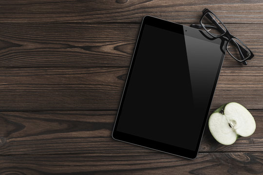 Half an apple, tablet PC, eyeglasses on old wooden background. Office table. Flat lay, top view