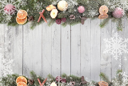 Christmas fir branches above and below with christmas fruits, white snowflakes as a border against a wood background 