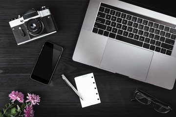 Workspace with notebook keyboard, camera, smartphone, eyeglasses on wooden background. View from above, office table desk