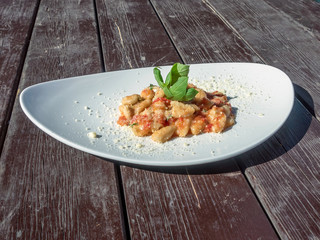 Italian gnocchi with b7asil on top on the curved plate. Wood table.
