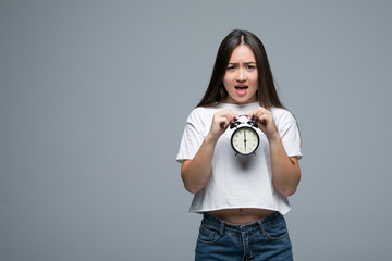 Fototapeta premium Sleepy shocked young Asian woman with a clock in the morning on gray background