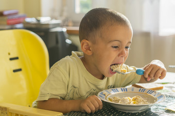 The boy 2 years eats porridge. Children's table. The concept of the child's independence. happy little boy eating porridge. Little boy eating breakfast at the table
