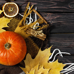 Orange pumpkin, cinnamon, slices of dried orange, autumn colorful leaves and checkered plaid on a dark wooden background top view with space for text. Autumn Pumpkin Thanksgiving Background.