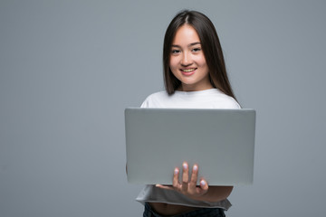 Naklejka premium Portrait of a smiling asian woman holding laptop computer isolated on gray background