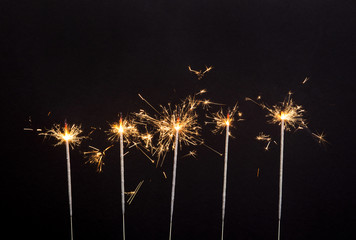 Burning sparklers in a row isolated on black background. Down border. 4th of July celebrations...