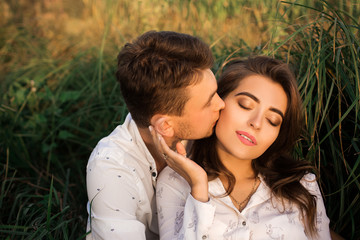 Young couple sitting in grass. A young man kisses a woman.
