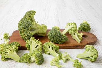 Chopped broccoli on a wooden cutting board on white wooden table, side view. Close-up.