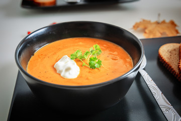 Pumpkin and carrot soup with cream and parsley in the black bowl
