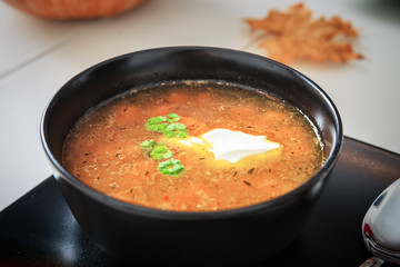 Pumpkin and carrot soup with cream and parsley in the black bowl