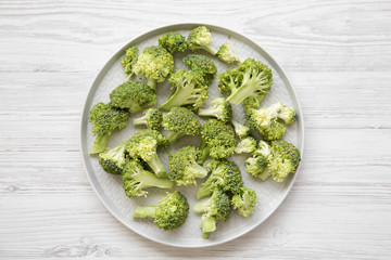 Freshly cut raw broccoli on gray plate over white wooden surface, overhead view. Flat lay, from above, top view.