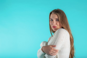 Pretty female with long hair, dressed casually in ivory sweater, looking with satisfaction at camera. Studio shot of good-looking beautiful woman isolated against blank turquoise studio wall. 