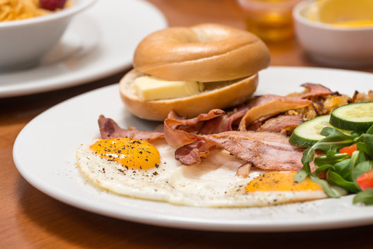 Delicious breakfast, fried eggs, bacon, bagel with butter.