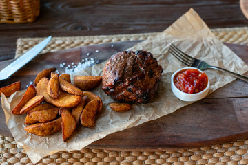 Filet Mignon with fried potatoes and tomato sauce on a wooden Board with Cutlery