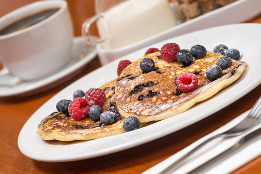 Delicious pancake with fresh fruit, blueberries and raspberries. Coffee and milk in behind.