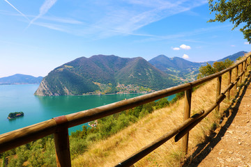 Fototapeta na wymiar Fence in foreground with panoramic view of mountain lake with island in the middle. Panorama from Monte Isola Island with Lake Iseo, Italy.