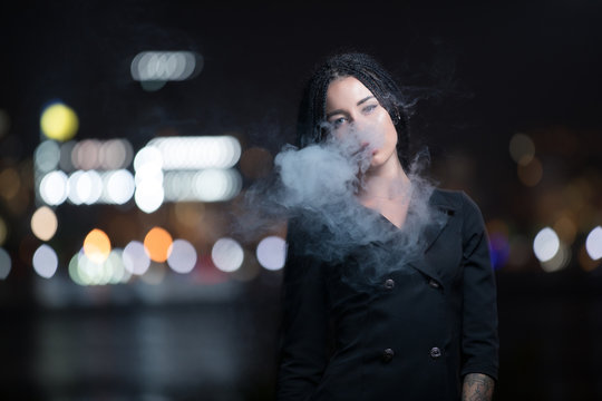 Woman smoking e-cigarette at night city lights