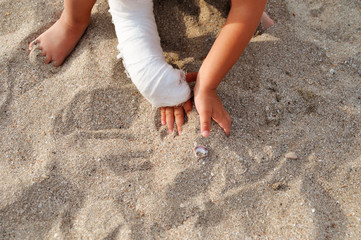Child with plaster on his hand playing in the sand on the beach by the sea.