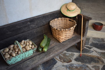 Cesta con patatas, calabacines del huerto y objetos antiguos sobre banco del siglo XVIII