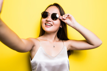Young cute asian girl making a selfie, standing on the bright yellow background and smiling