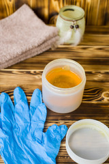 jar of sugar paste for sugaring, razor, blue gloves,  towels are on wood background (vertically)