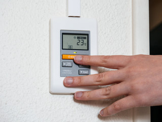 Press start to turn on - hand adjusting a wall mounted thermostat temperature for the room AC air conditioning system - fan speed and temperature up down button.