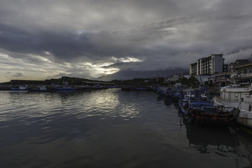 Fishing Boats docked in Chenggong Harbor, Taitung County, Taiwan. Evening time with sun beginning to set in the background, row of blue boats and water in the foreground. Sea Vessels, Calm Water