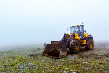 The yellow bulldozer on pale green ground in fog