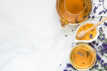 lavender tea in a cup and teapot with honey and fresh flowers over white marble table. herbal...