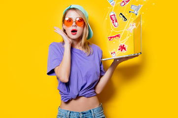 Young style girl with orange glasses and laptop and gifts computer on yellow background. Clothes in 1980s style