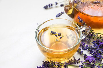 cup of lavender tea and teapot with fresh flowers over white marble table. herbal drink. close up