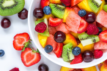 Fruitsalade met watermeloen, aardbei, kers, bosbes, kiwi, framboos en perziken in een kom op witte achtergrond