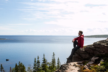 Fototapeta na wymiar Young bearded guy in tourist clothes looking out into the distance against a blue lake