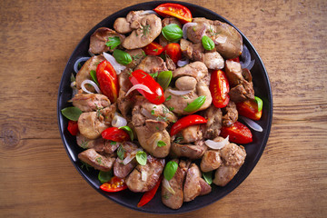 Chicken liver with  tomatoes, onions and basil on black plate, wooden table. overhead, horizontal