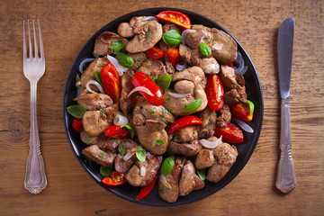 Chicken liver with  tomatoes, onions and basil on black plate, wooden table. overhead, horizontal