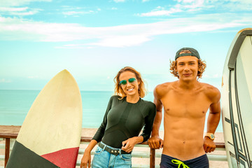 Obraz premium Smiling young active couple surfers relaxing on the beach after sport with Surfboard. Healthy Lifestyle. Extreme Water Sports