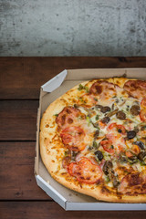 Pizza on wooden background in rustic style. Italian pizza from the shop in a cardboard box. Simple food on a wooden background