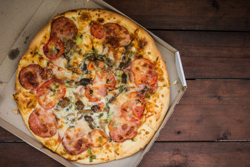 Pizza on wooden background in rustic style. Italian pizza from the shop in a cardboard box. Simple food on a wooden background