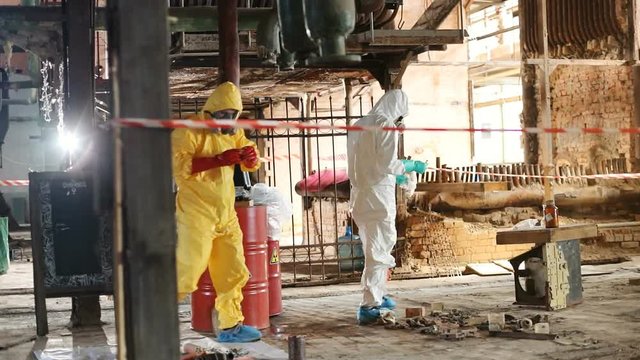 Two young Caucasian scientists in colored hazmat suits working together in abandoned nuclear power station. Dangerous job. Environment.