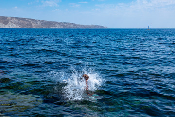 A boy is jumping from the cliff into the sea wiht big water splash on a hot summer day. Holidays on the beach. The concept of active tourism and recreation