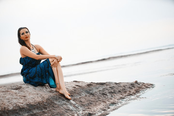 Beautiful woman sitting on big stone in the sea. Harmony and meditation concept. Healthy lifestyle