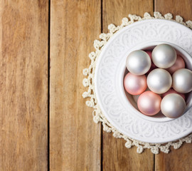 Beautiful small Christmas tree ornaments white pink pearl red balls in vintage ceramic cup on sauces lace napkin. Weathered plank wood background. Warm colors. Holiday poster card copy space